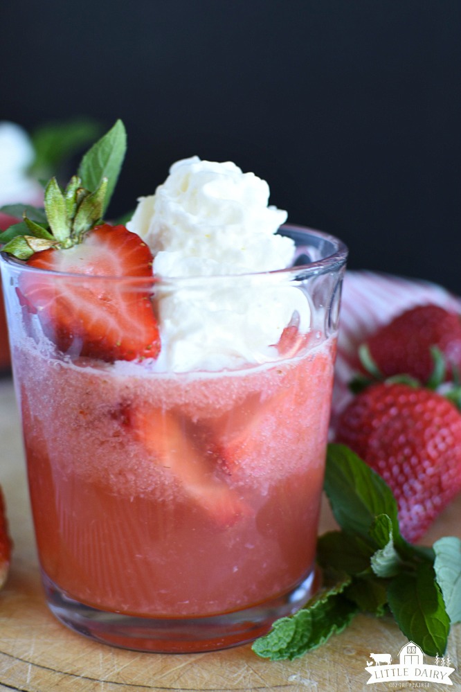Strawberry drink in a glass with a sliced strawberry and whpped cream on top