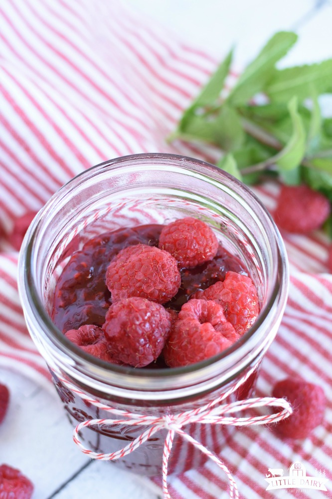 a canning jar with raspberry sauce and fresh raspberries on top, on a red and white striped napkin