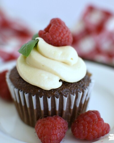 chocolate cupcakes with cream cheese frosting piped on top and a fresh raspberry