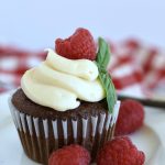 chocolate cupcakes with cream cheese frosting piped on top and a fresh raspberry