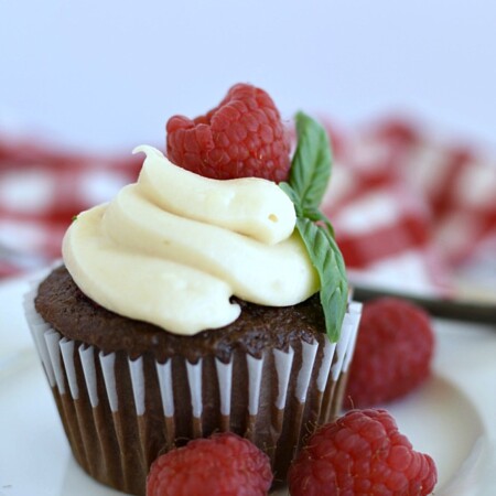 chocolate cupcakes with cream cheese frosting piped on top and a fresh raspberry