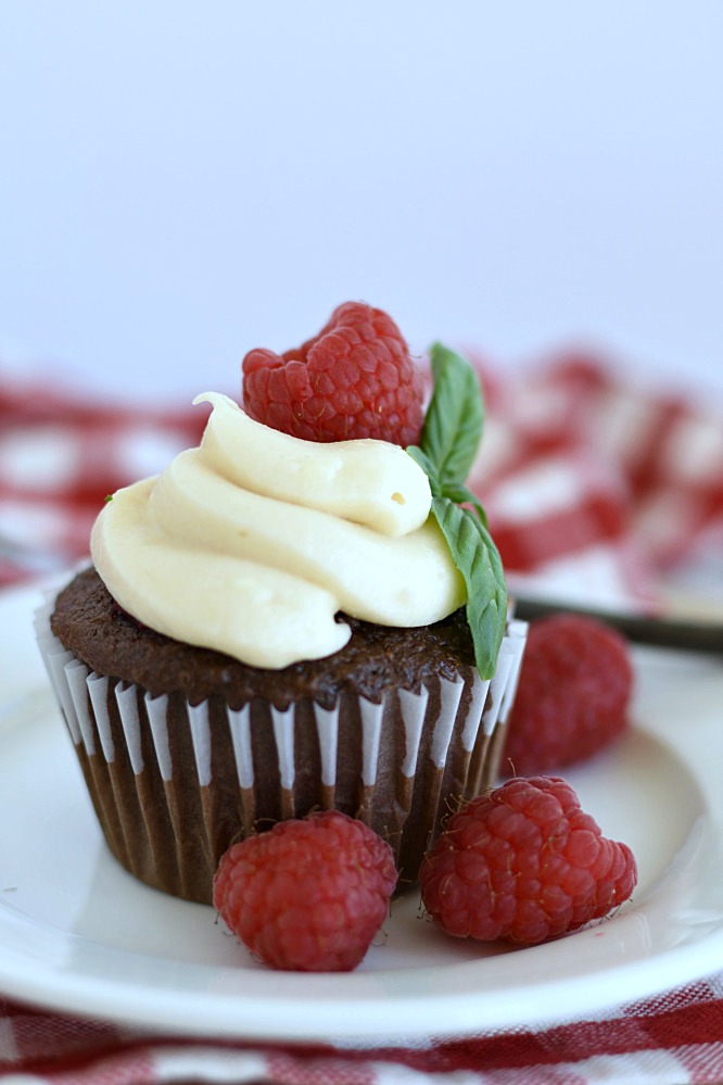 chocolate cupcakes with cream cheese frosting piped on top and a fresh raspberry