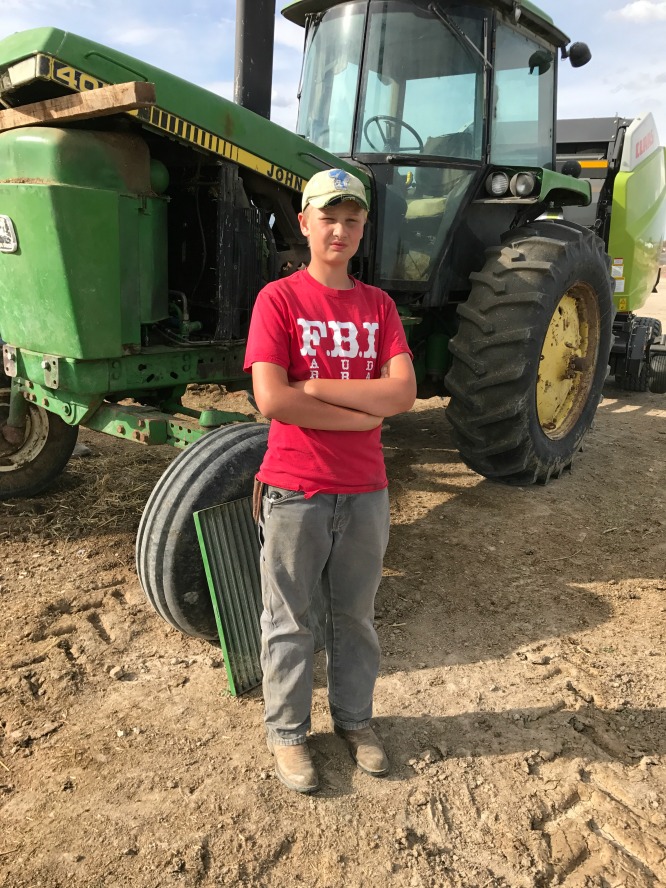 A boy in a red shirt standing in front of a john deere tractor