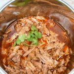 shredded pork roast in a pressure cooker in red liquid