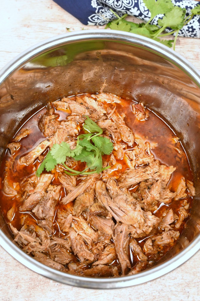 Shredded pork roast in a pressure cooker in red liquid.