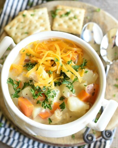 Cheesy Chicken Potato Soup in a white bowl with crackers on a plate