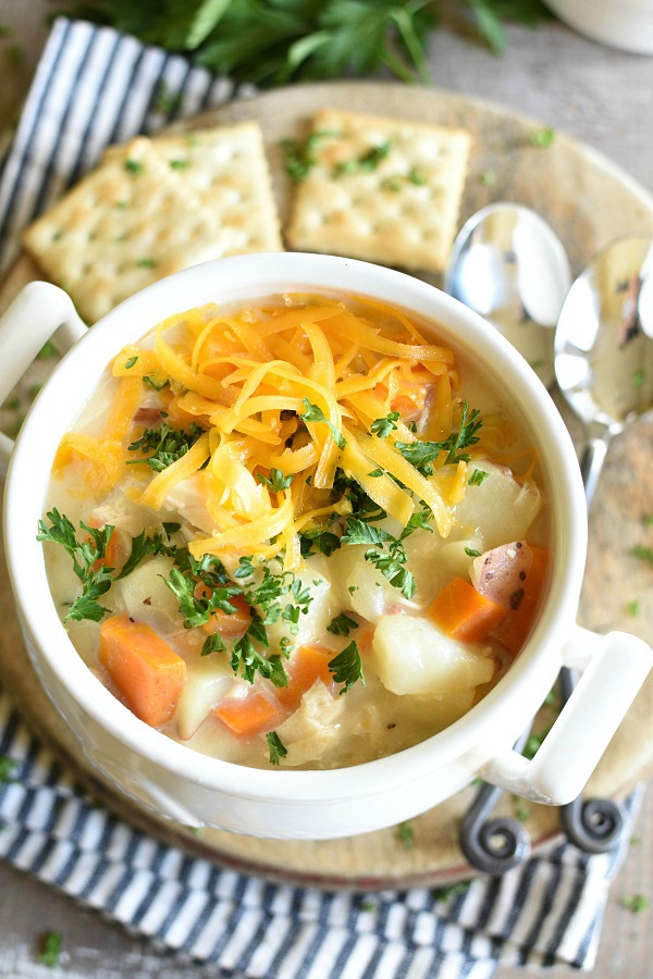 Cheesy Chicken Potato Soup in a white bowl with crackers on a plate