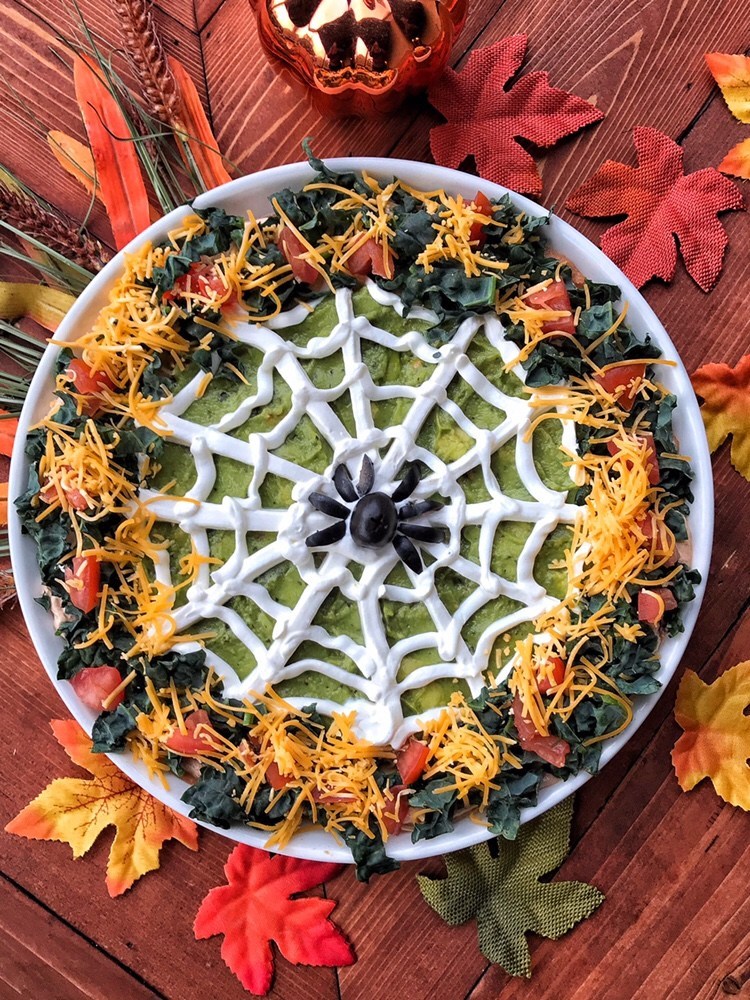 taco dip with layers of avocado dip, and decorated with a sour cream spider web