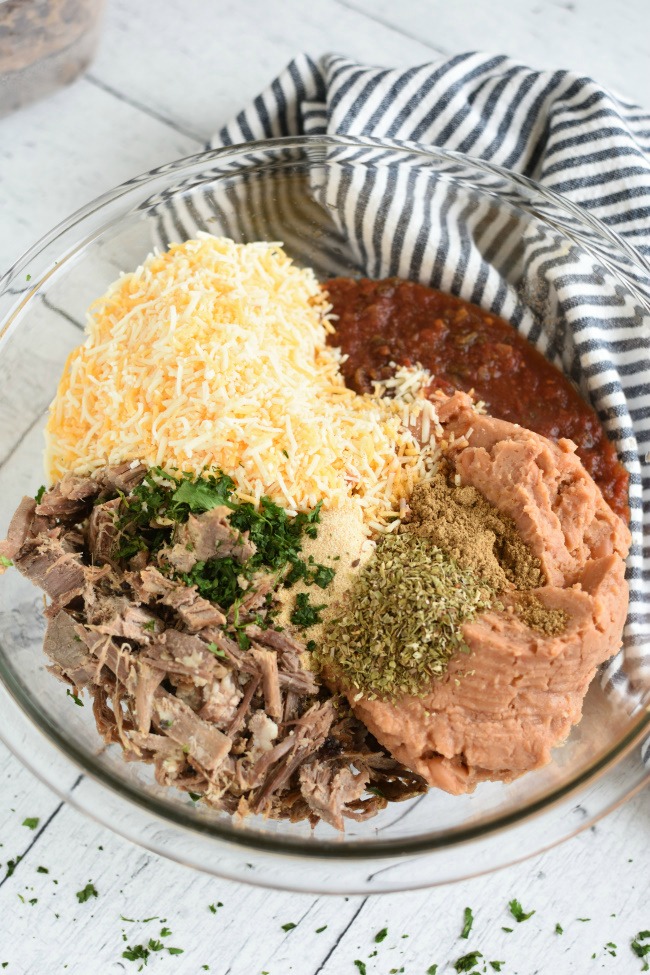 Shredded roast beef, burritos, shredded cheese, and spices in a bowl