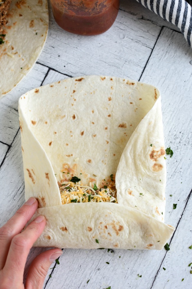 Flour tortilla with beef and bean filling being rolled up