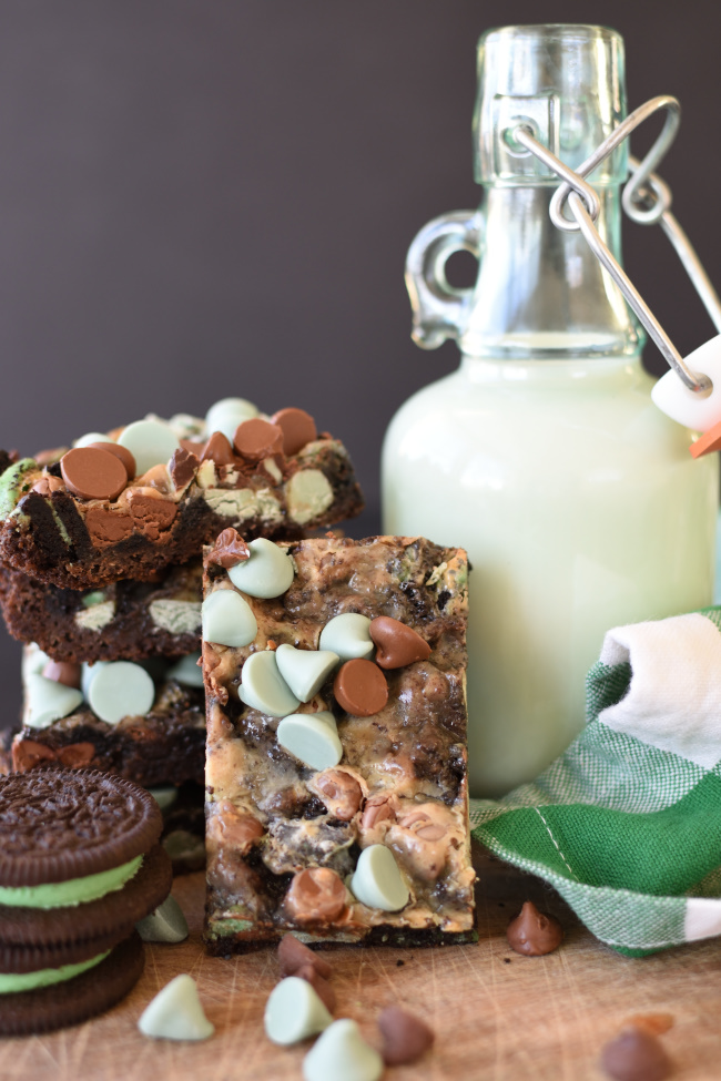 Mint Chocolate Magic Bar Cookies on a board with a container of milk and mint chocolate sandwich cookies
