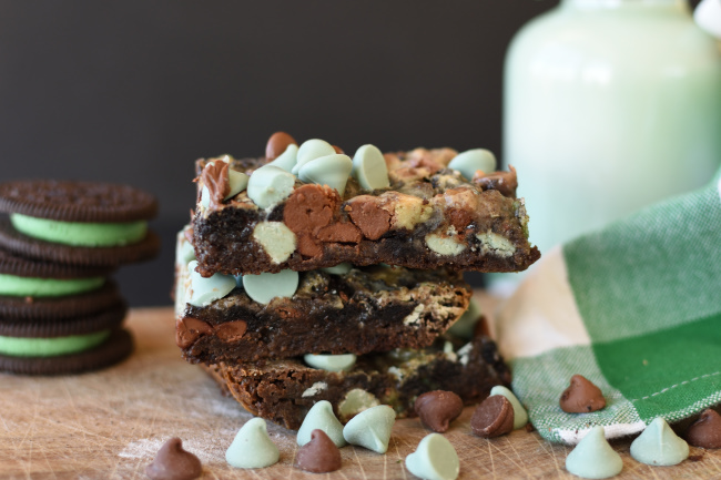 A stack of mint chocolate magic bars with a container of milk and a green and white napkin