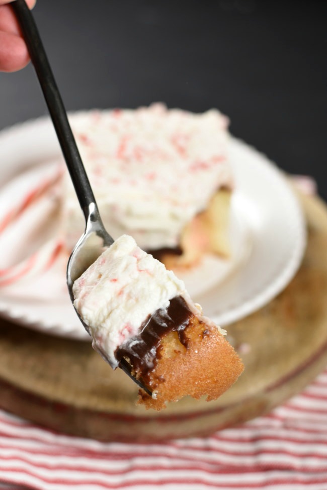 a fork with a bite of white cake, a layer of chocolate fudge sauce, and whipped cream frosting