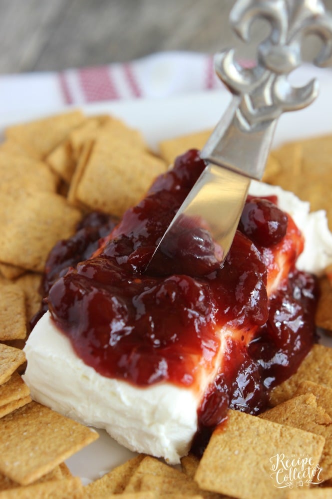 a brick of cream cheese spread with cranberry sauce with wheat crackers for serving