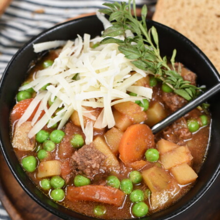 a black bowl with beef stew topped with cheese and herbs