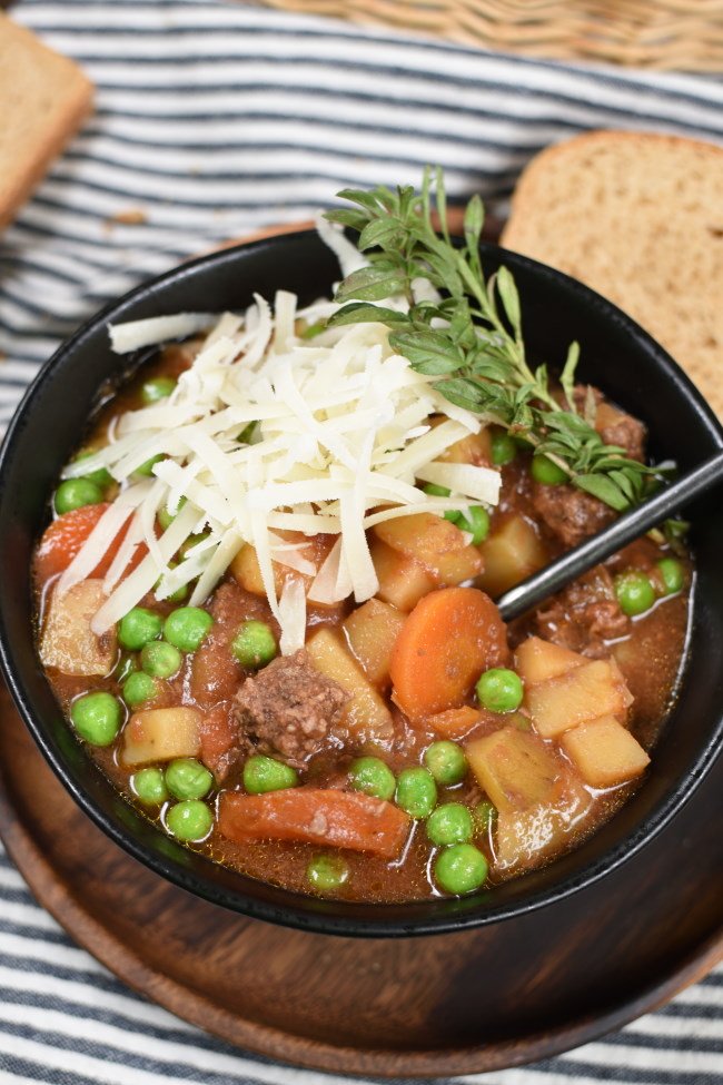 a black bowl with beef stew topped with cheese and herbs