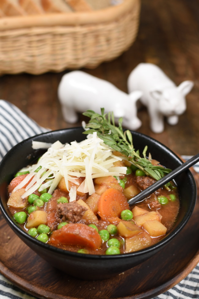 a black bowl with beef stew topped with cheese and herbs