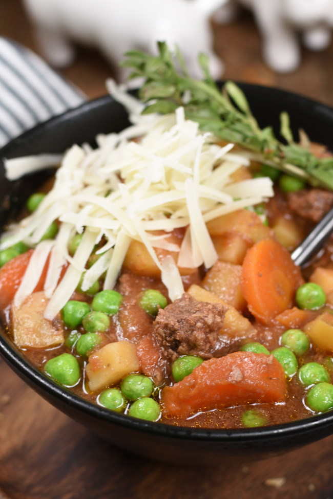 a black bowl with beef stew topped with cheese and herbs