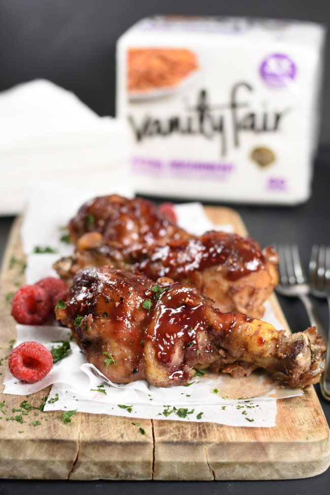 glazed chicken drumsticks on a parchment lined board with raspberries scattered around