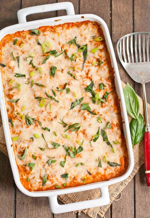 a white baking dish with baked cheesy casserole, sprinkled with fresh basil