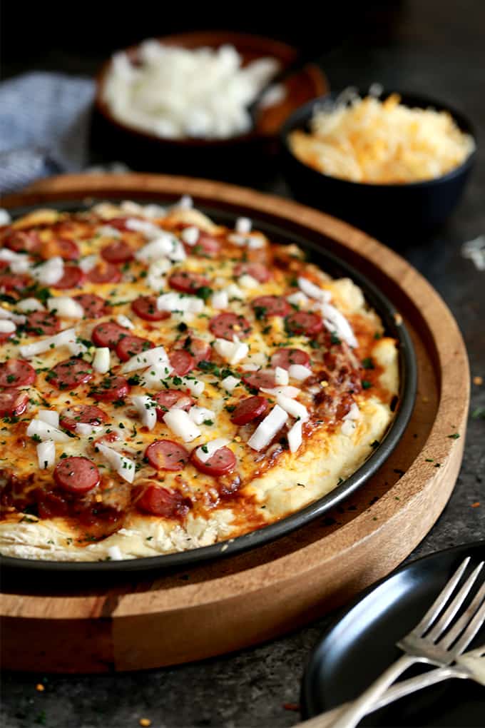 A round pizza pan with baked pizza with sliced hotdogs, cheese, and onions