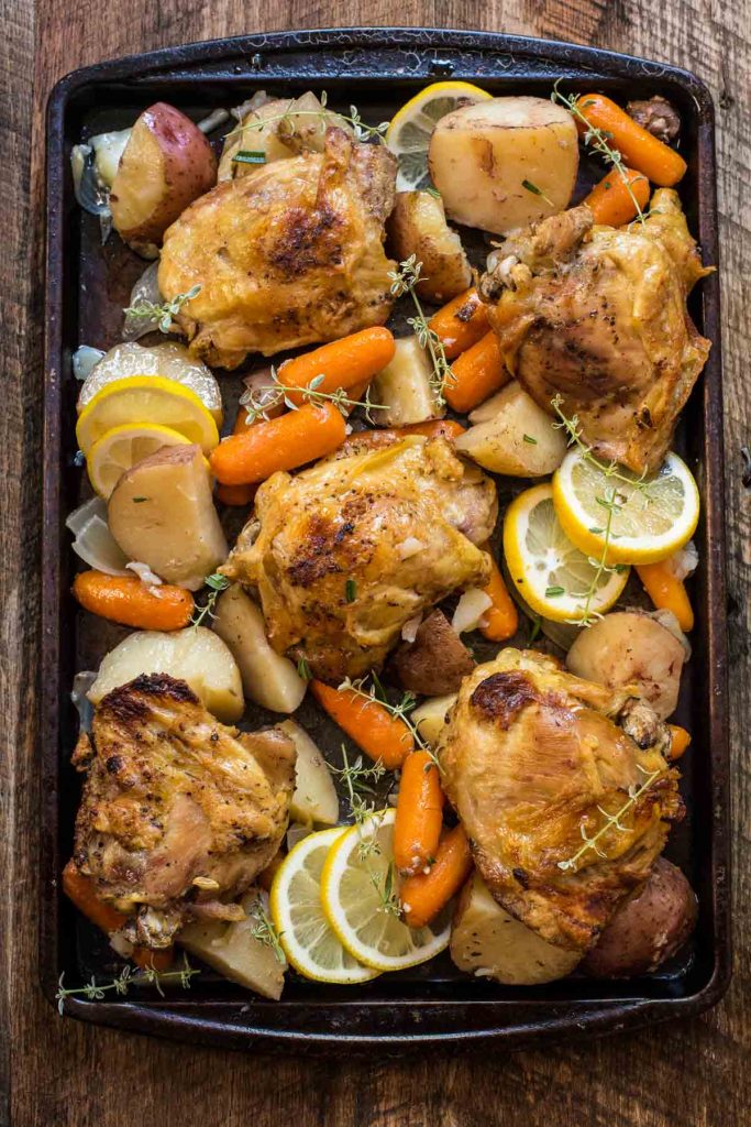 baked chicken and vegetables on a baking sheet with sliced lemons