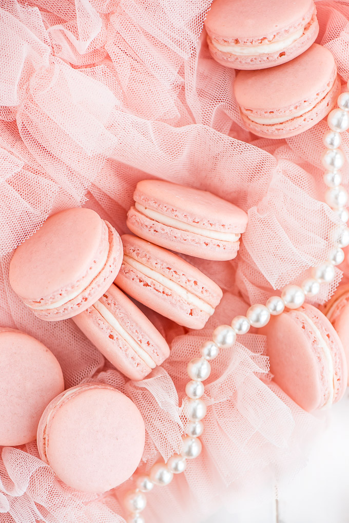 pink macarons with pink icing in the middle on pink netting and pearls