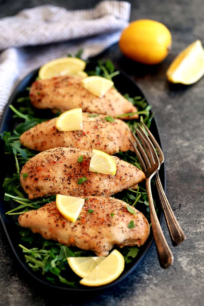 a platter with four cooked chicken breasts with lemon on top