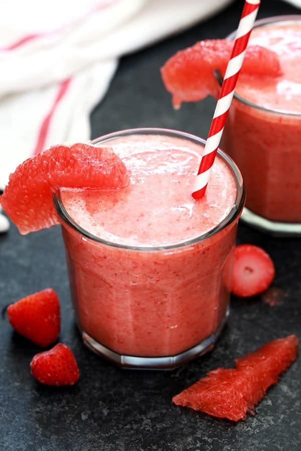 a red smoothie with a red and white drinking straw and a grapefruit section hanging over the edge of the glass