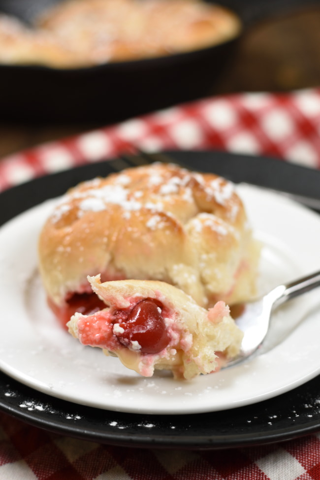 one piece of baked cherry cheesecake monkey bread on a plate with a bite on a fork