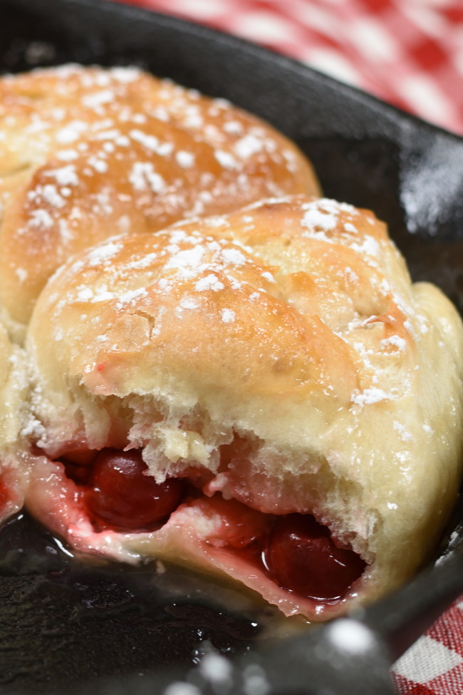 A cherry cheesecake bomb in a cast iron skillet, dusted with powdered sugar