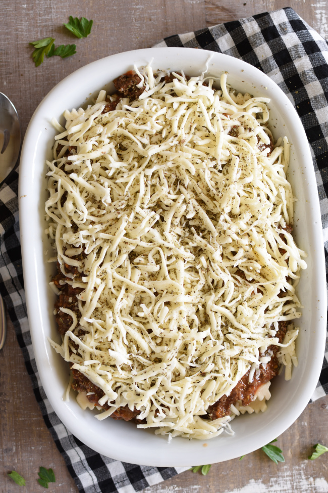 shredded mozzarella cheese sprinkled over ground beef in a white baking dish