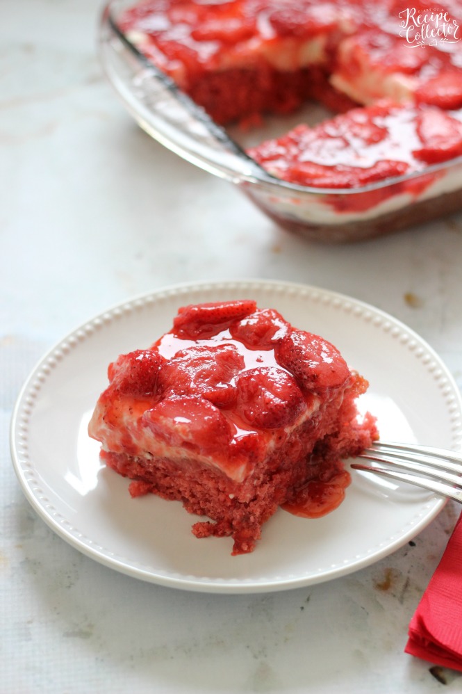 a square of strawberry cake on a white plate, topped with whipped cream and strawberries