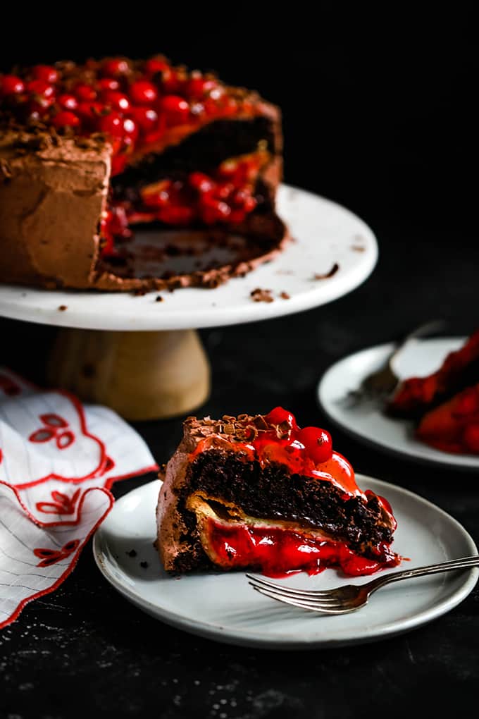 a wedge of chocolate pie stuffed with cherry pie, and a cake stand of cake in the background