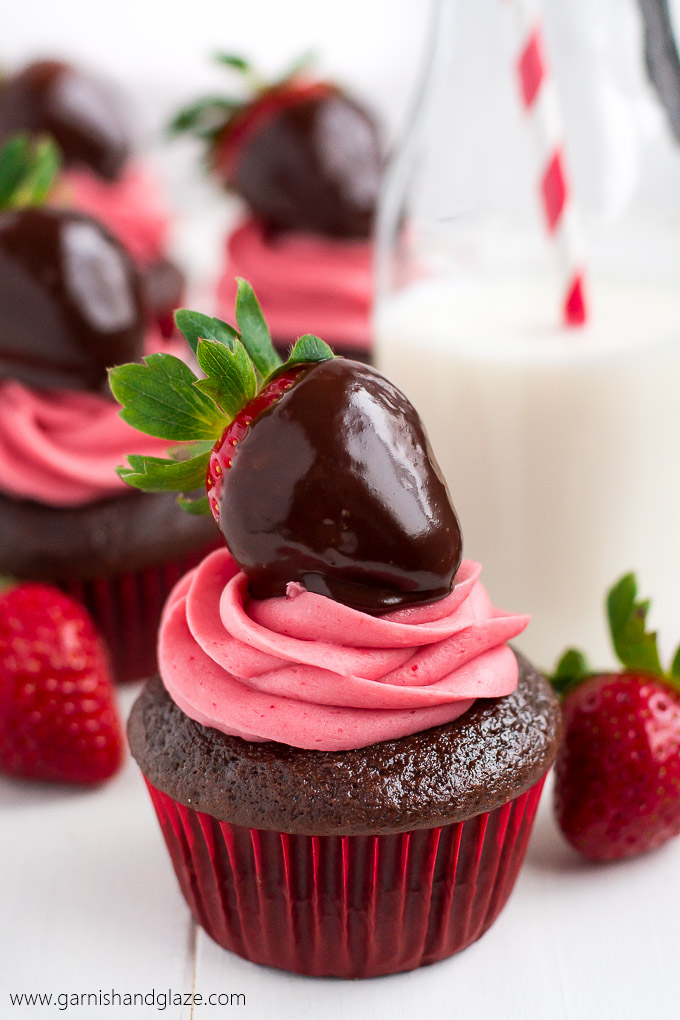 A chocolate cupcake piped with pink icing and topped with a chocolate covered strawberry.