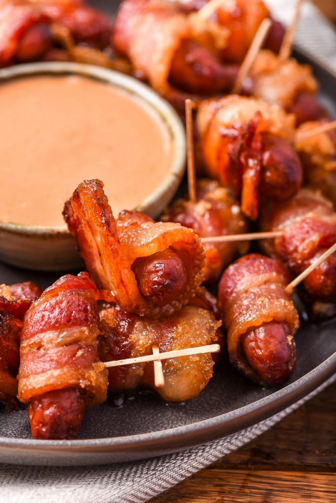 A tray with bacon wrapped smokies with toothpicks, and a dish of pink sauce in the  middle