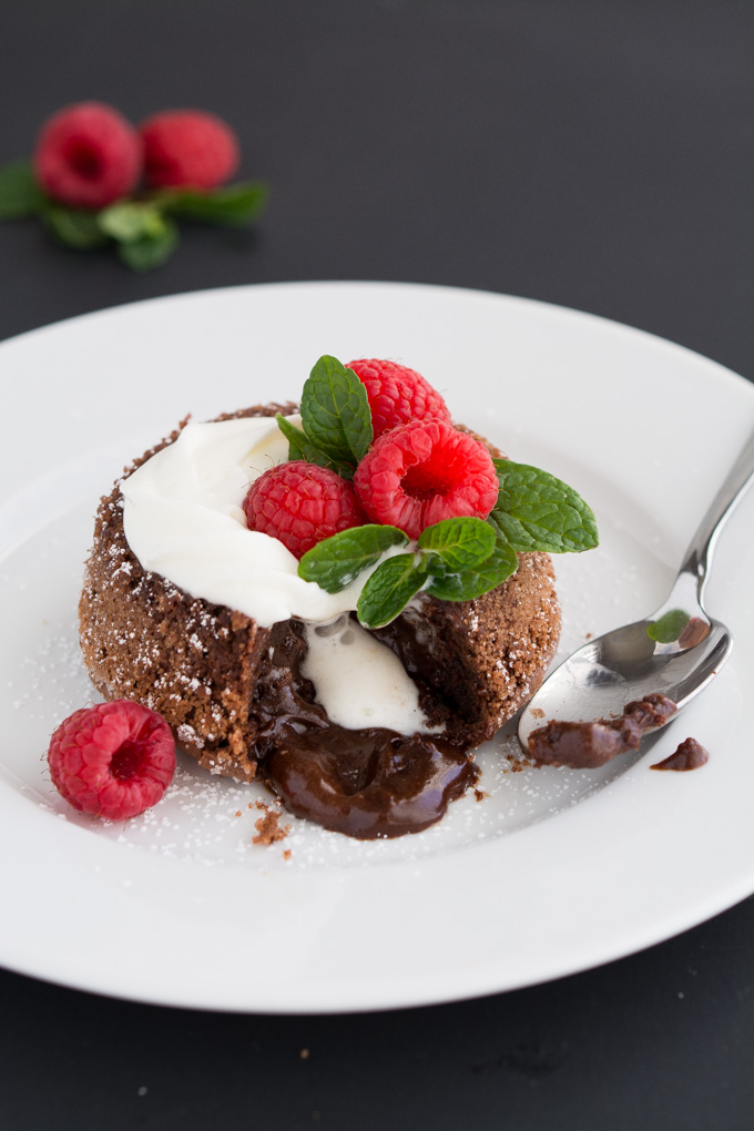 A chocolate molten cake topped with whipped cream, fresh raspberries, mint leaves and whipped cream