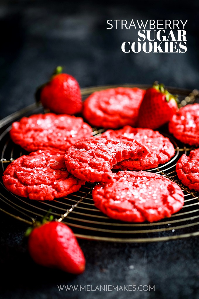 red sugarcookies on a round, black cooking rack with strawberries scattered around