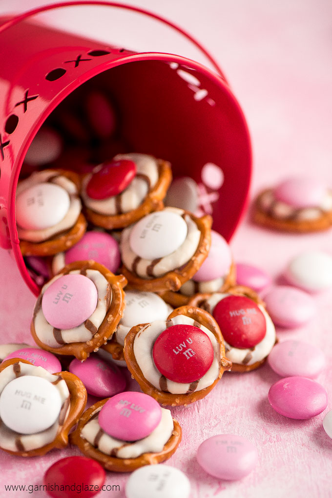 a red pail filled with pretzels topped with a melted striped hug and pink and red candies