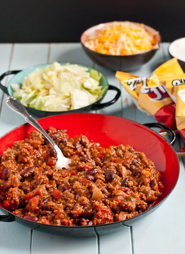 bowls filled with taco meat, sliced lettuce, grated cheese, and a bag of corn chips