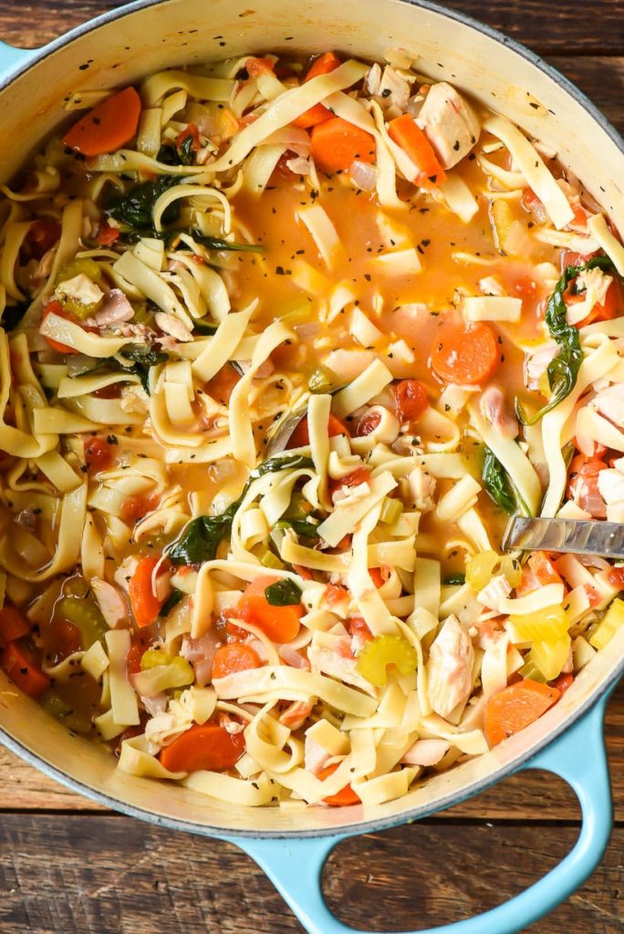 A pot of chicken noodle soup with kale, carrots, and celery