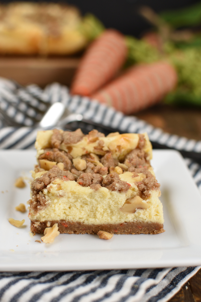 a square of cheesecake on with carrot cake stressel and chopped walnuts