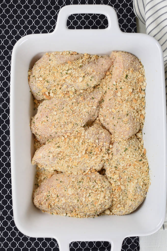 a white baking dish with breaded and unbaked chicken breasts