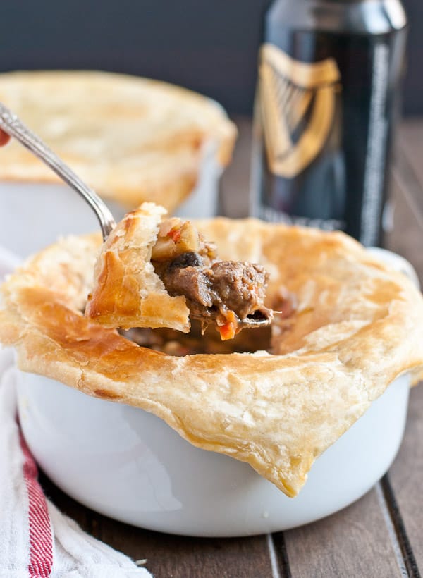 a spoon dipping into a bowl filled with pot pie, topped with a puff pastry crust