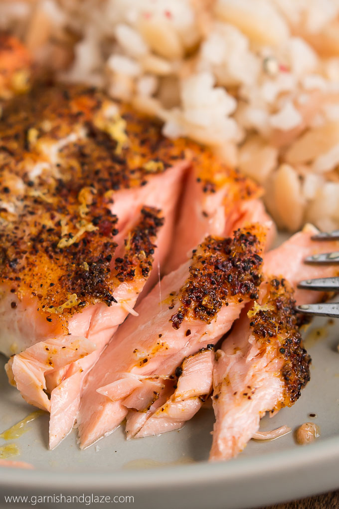 a fork pulling a baked piece of pink,  seasoning topped salmon apart