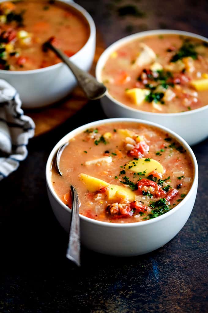 three bowls of soup in a red creamy sauce with vegetables
