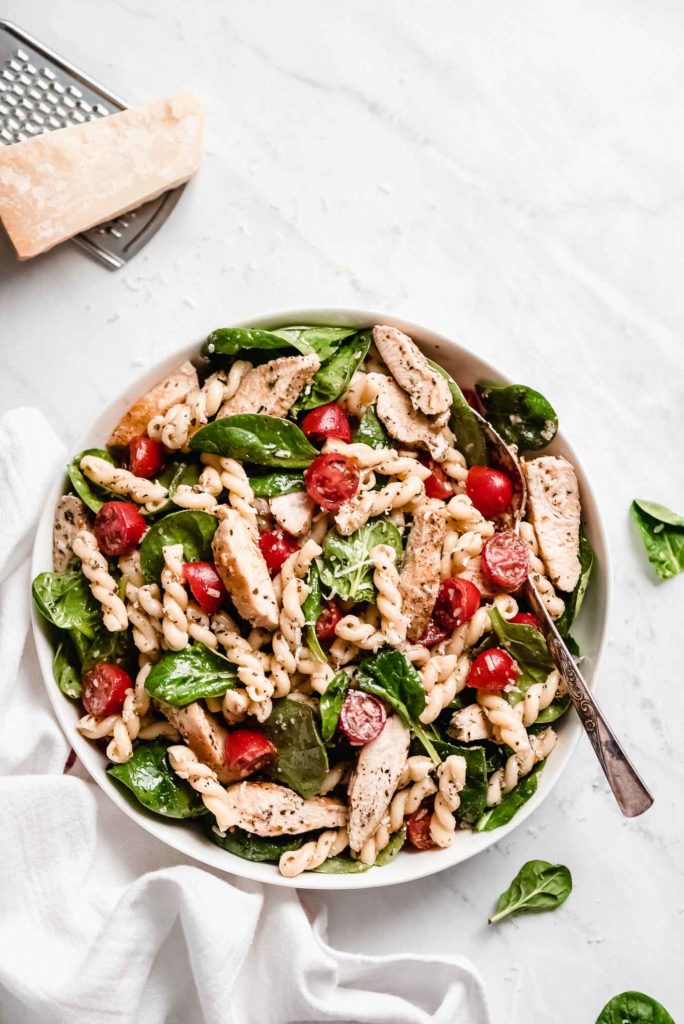 a dish of pasta salad with fresh spinach and cherry tomatoes