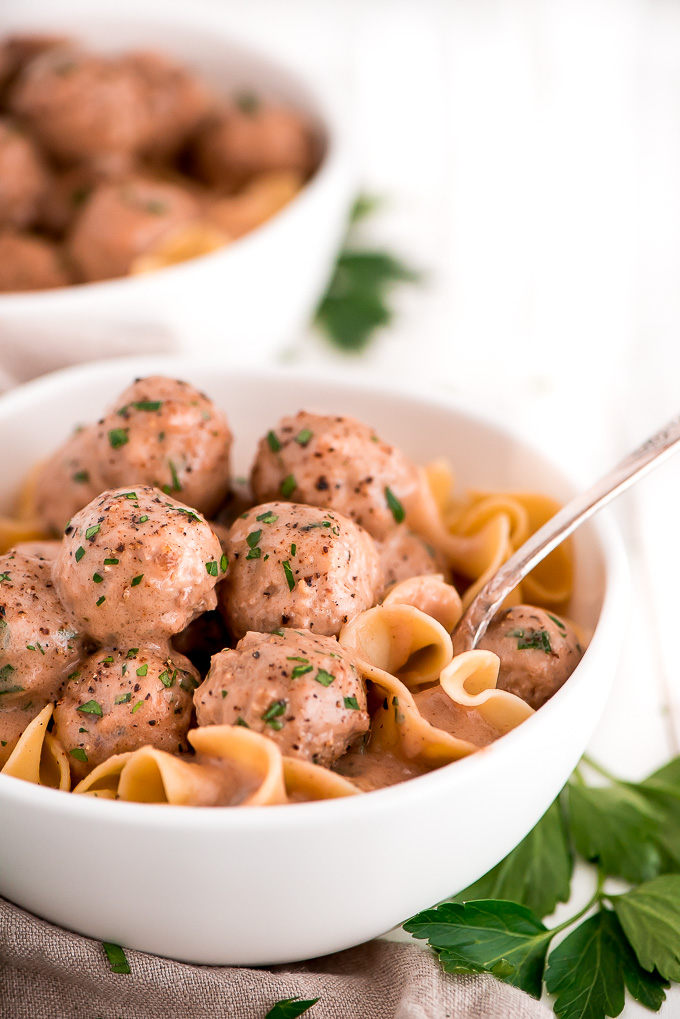 meatballs and gravy over pasta, sprinkled with chopped parsley