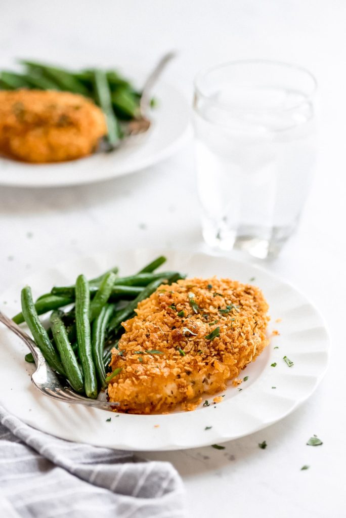 a baked, cornflake coated chicken breast and green beans on a plate