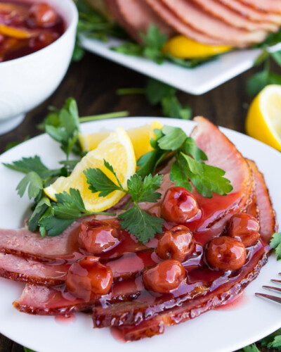 a plate with sliced ham, topped with cherries, a lemon wedge and parsley